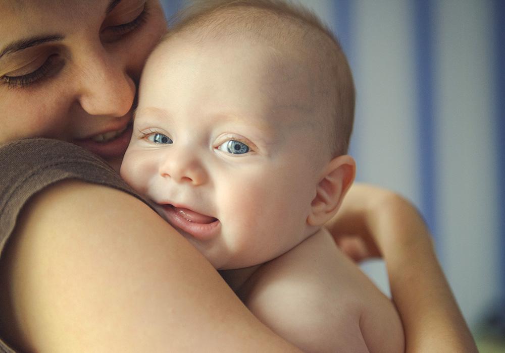 A mother holding a baby to her shoulder as the baby looks into the camera
