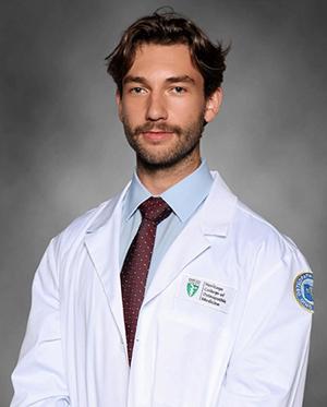 Nick Shonkwiler wearing a Heritage College white coat, light blue dress shirt and patterned tie.