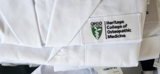Close-up of white coats with Heritage College of Osteopathic Medicine logo embroidered on them