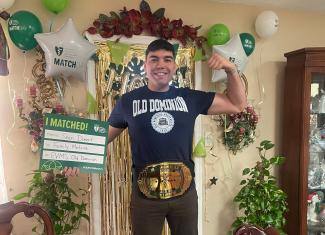 Graduate Sean Diment holding Match Day sign and wearing wrestling belt
