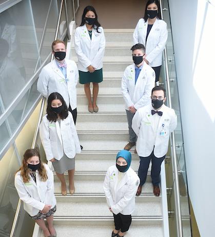 Medical students wearing their new white coats line a staircase