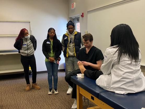 Three Aspiring Doctors students watch a presenter explain how to treat a foot injury.