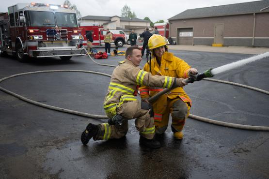 A Heritage College student uses a fire house with a firefigher during Disaster Day