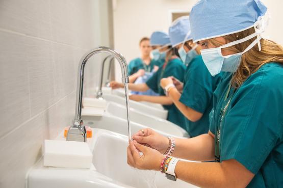 Three medical student wearing scrubs in a line wash their hands 