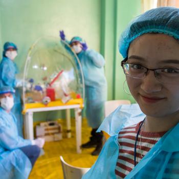 A student in lab gear smiles and 4 people pose in the background