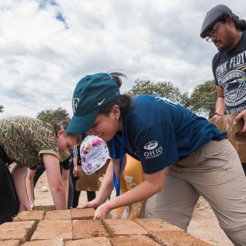 A group of volunteers moves blocks to build a house in Bellamaria Community