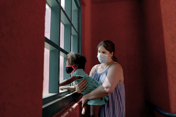 Kristina Woldan, a frontline nurse, holds her daughter Zoe up to a window at the Los Angeles Zoo. Photo by Erin Burk for "Biding Time"