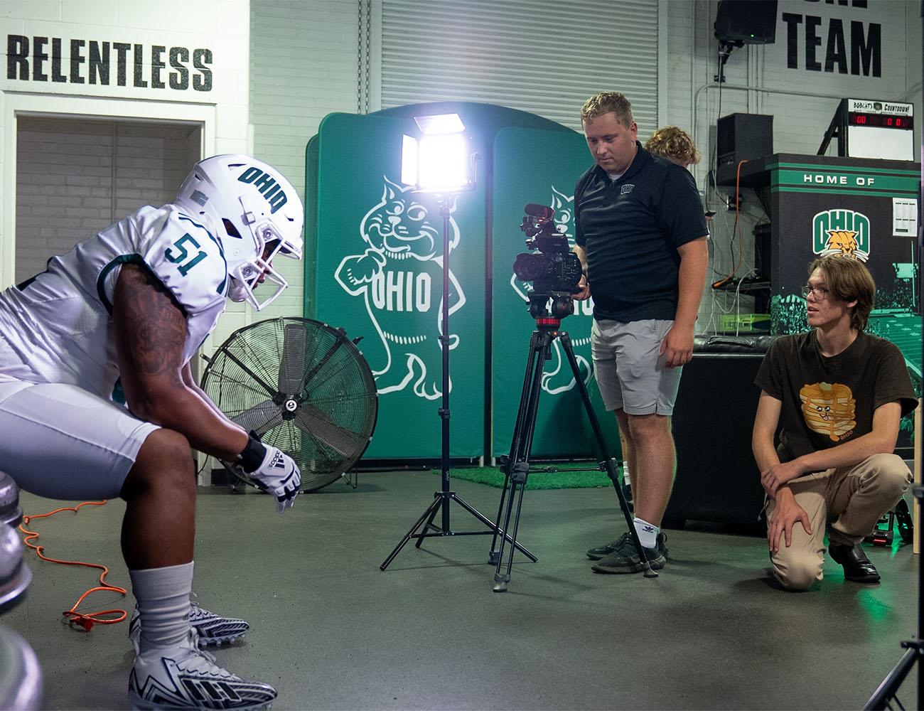 A student assists with a photoshoot for the OHIO football team.