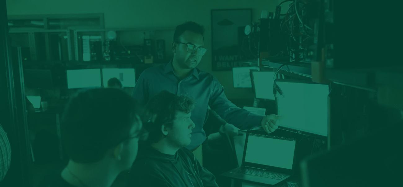 A professor works with students on computers