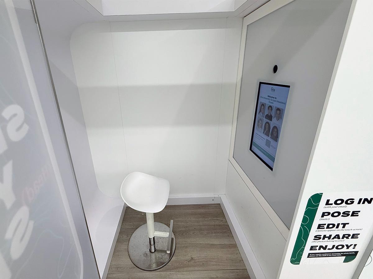 Inside the headshot booth: a small stool faces a touch screen display with a camera above.