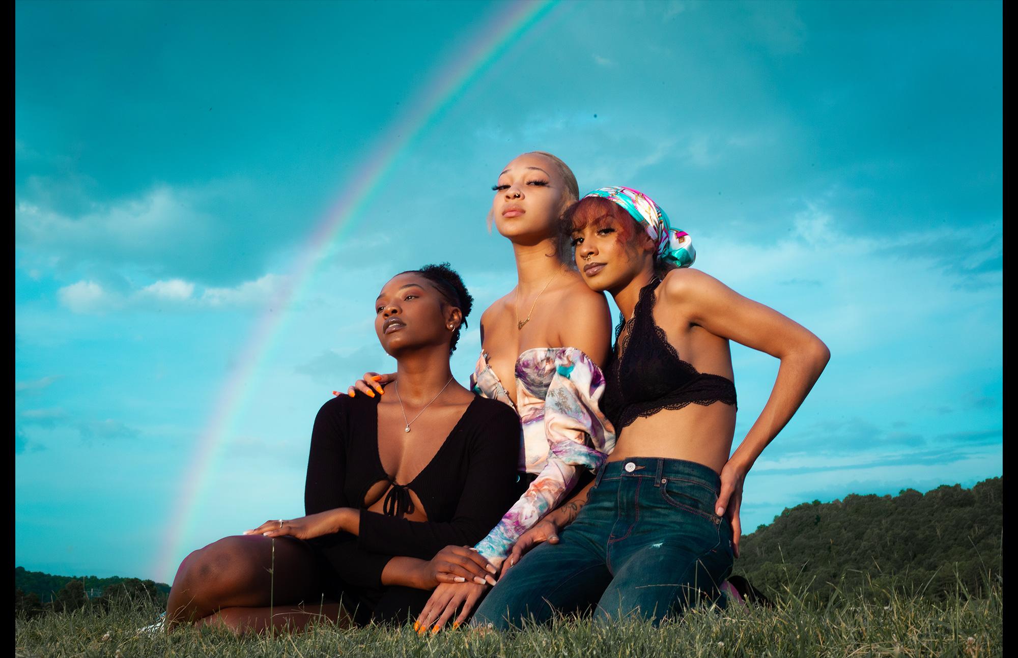 three women in field with rainbow