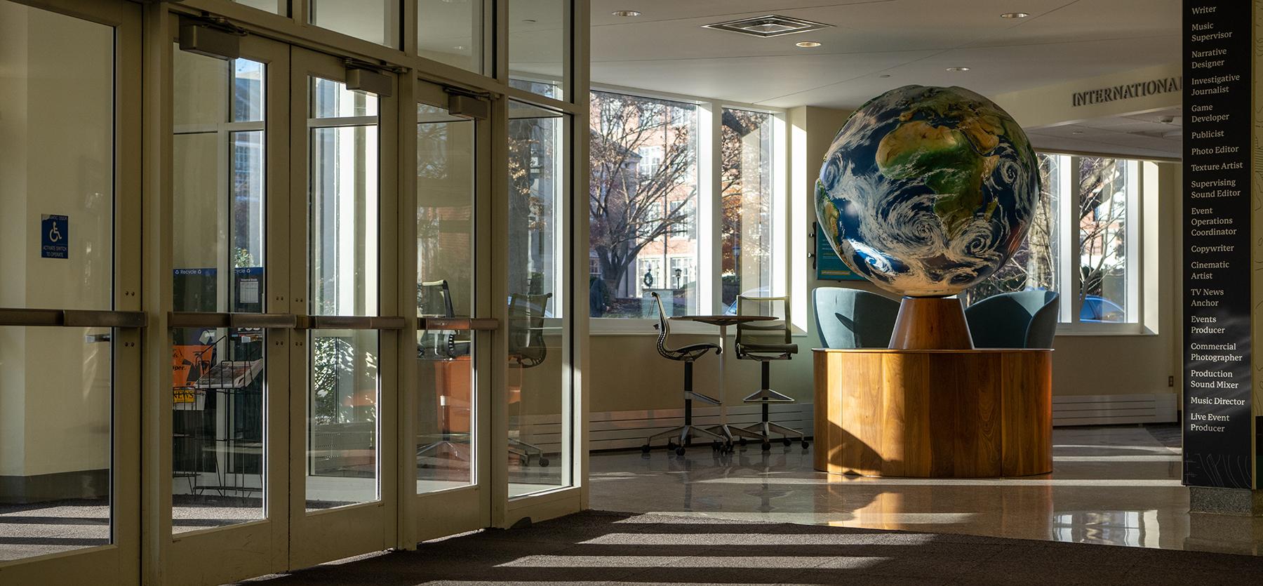 The lobby of the Schoonover Center, which houses the Scripps College of Communication, featuring light filtering in the doors and a giant globe
