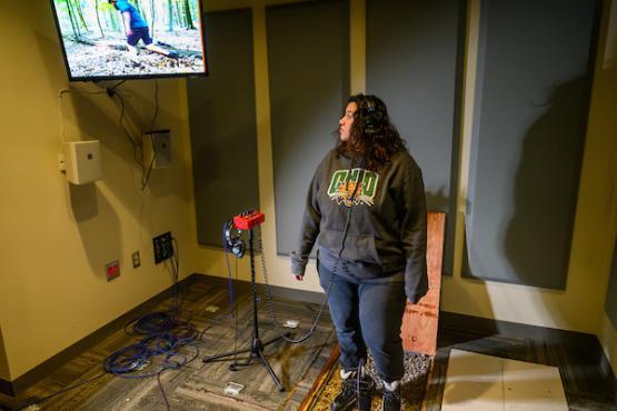 woman standing wearing headphones while looking at a video