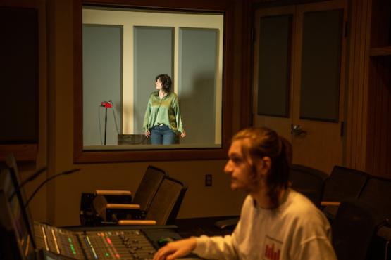 Student records sound effects in one room with another student monitoring equipment next door in OHIO's post production audio studio