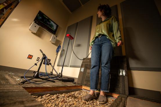 Student stands on rocks while recording sound effects in OHIO's post-production audio studio