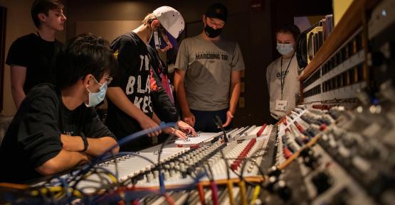 People working on a mixing console in a recording studio