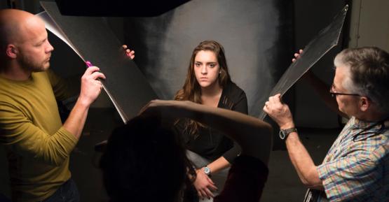 Woman get's photograph taken while two people on both sides of her hold up light baffles