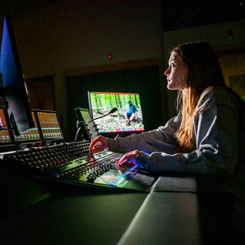 An Ohio University student in front of multiple screens in a media lab