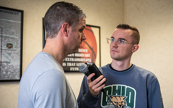 Jake Hromada, a senior in the Scripps College of Journalism, interviews a man with a microphone.