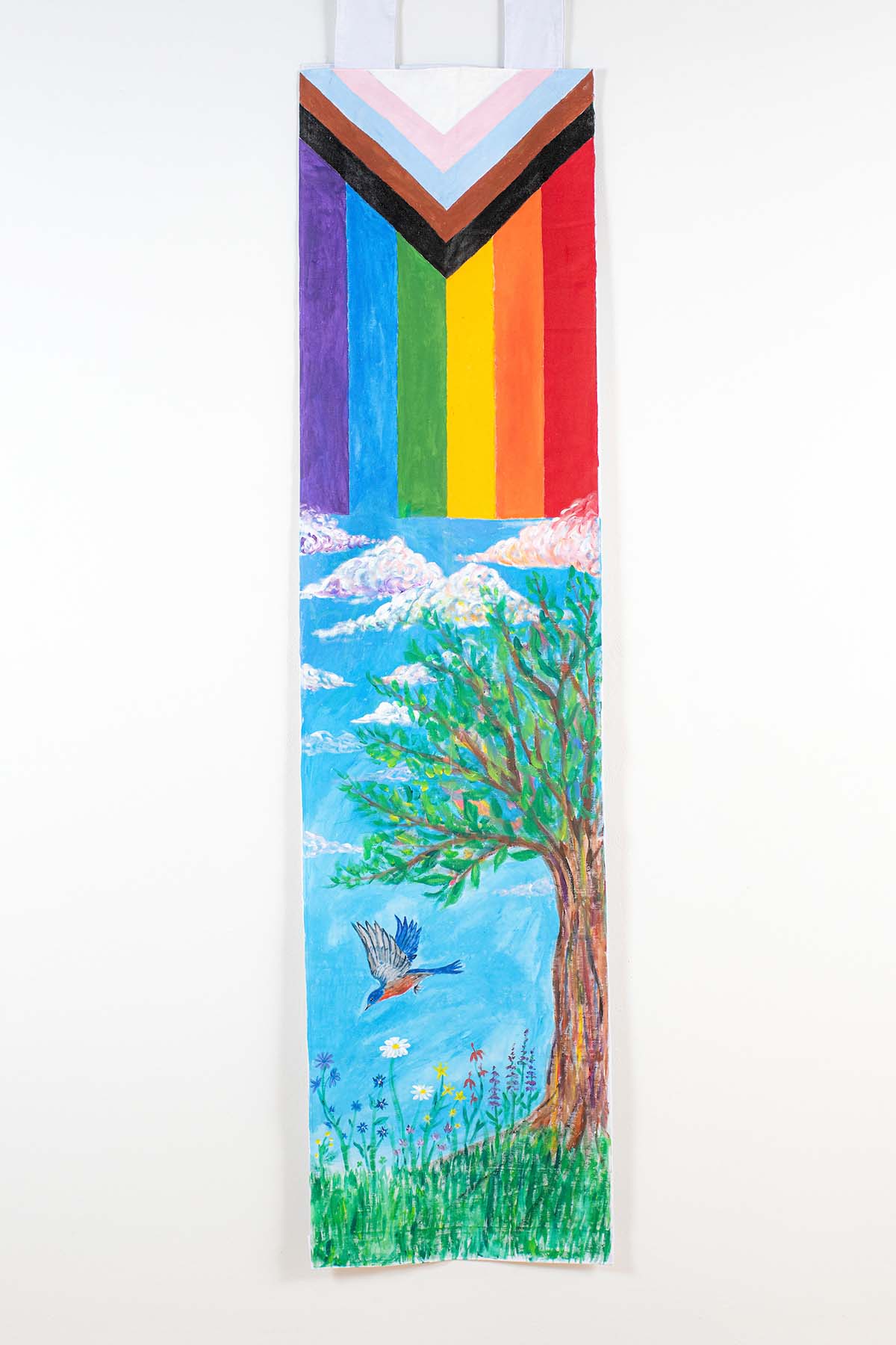 Photo of an art piece depicting a vertical rainbow block atop a dreamy blue sky and a blue bird diving down past flowers from a blooming tree
