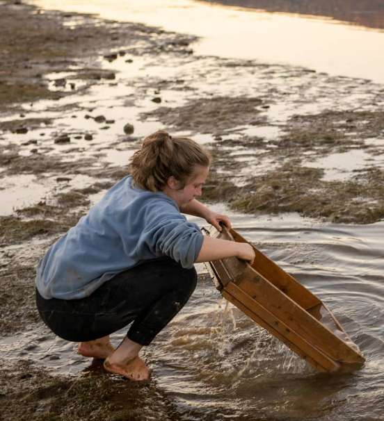 Student sifting soil in shallow river