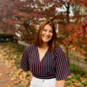 Breanna Reidl during autumn, wearing a vertically red and pale blue striped shirt and a pair of white pants.