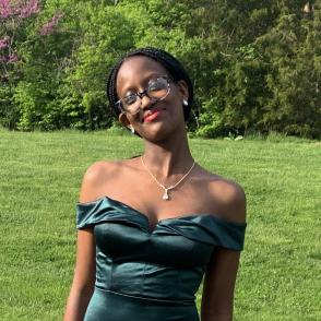 An image of Divine Mbabazi in a formal dark green silk dress. A green field is in the background.
