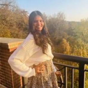 Krupaben Patel standing with hills in the background, wearing a white sweater and a floral skirt.