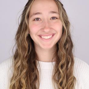 Hayleigh Harr stands in front of a white wall with a lighter white sweater on, smiling.
