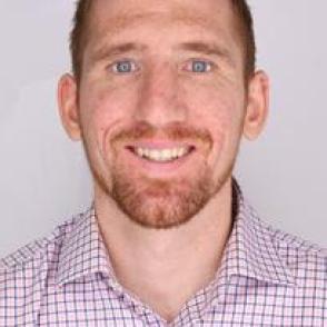 headshot of Jake Lietzow. a white male with facial hair and short reddish brown hair smiling facing the screen. Wearing a red and white checkered shirt 