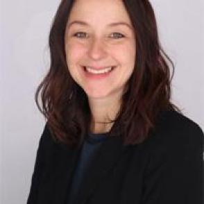a white woman smiling facing the camera with dark shoulder length hair wearing a black top and a black blazer