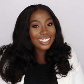 an African American woman with dark shoulder length hair facing the screen smiling, wearing a black top and a white blazer
