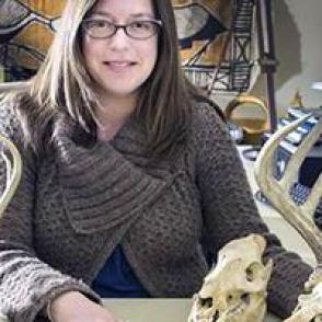 Sabrina is wearing a brown cardigan and sitting down by a desk