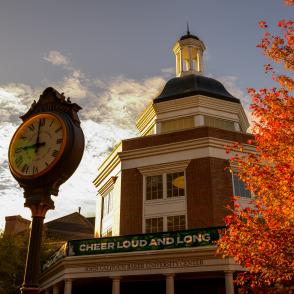 Clock and brick building with cupola at Ohio University’s Baker Center, framed by bright autumn leaves under a partly cloudy sky.