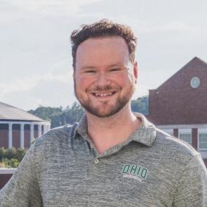 a man wearing with short brown hair, a mustache, and short beard smiling 