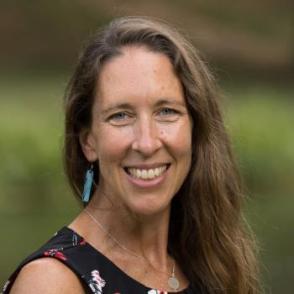 a woman smiling wearing a sleeveless top with long light brown hair and dangling earrings