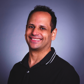 a man smiling with short dark hair wearing a black polo shirt 