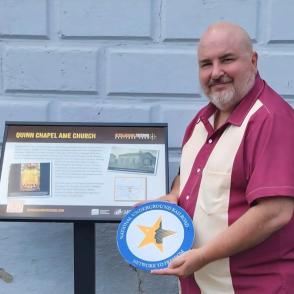 man standing in front of signage holding a National Underground Railroad Network to Freedom emblem