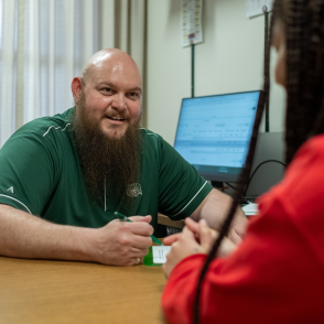Man at desk holding pencil and talking with student