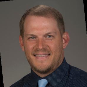 A photo of a man in a dark shirt with a blue tie