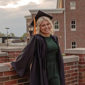 Woman in cap and gown smiling with brick building in background