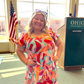 woman in brightly colored dress smiling with hands on hips