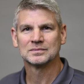 image of a White male with shorter grey hair combed to the side wearing a charcoal grey polo shirt 