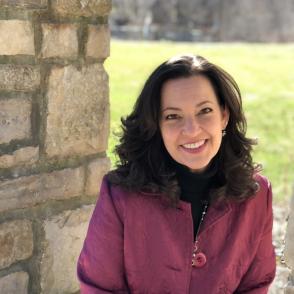 image of a White woman with shoulder length dark hair wearing a magenta colored suit