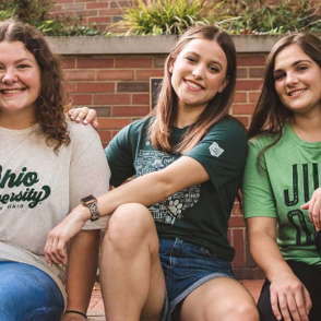 Three girls sitting wearing Ohio is Home t-shirts smiling at camera.