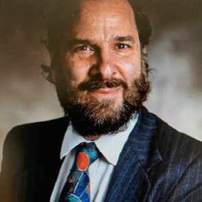 image of a male with a beard and dark hair smiling wearing a dark suit with a colorful tie