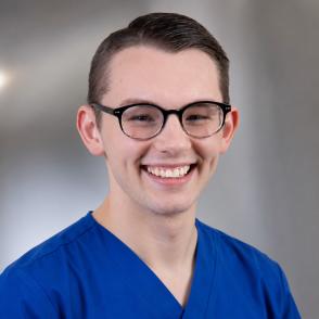 Cody Stephens smiling in portrait, wearing scrubs and glasses