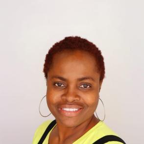 image of a woman smiling wearing a yellow shirt with black overalls and hoop earrings 