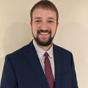 A photo of a man in a suit in front of a tan background
