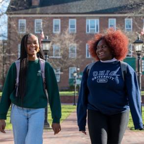 two peer leaders connect and take a walk on college green talking and smiling